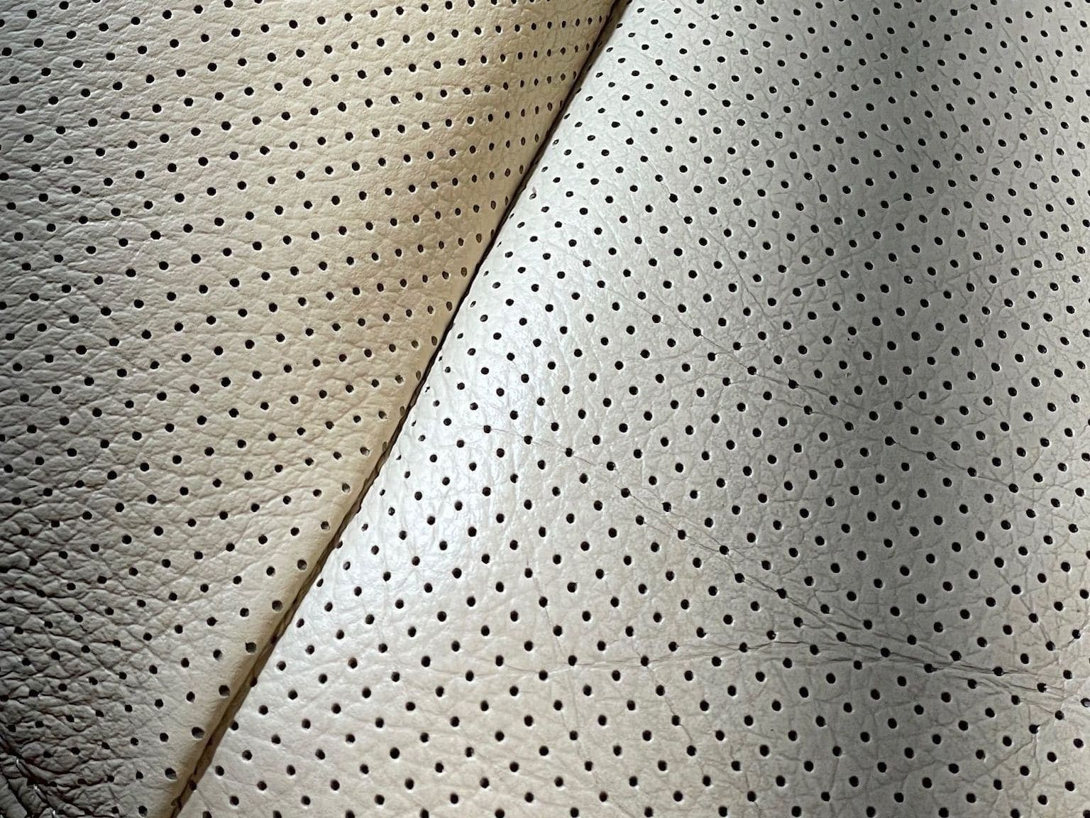 Close-up of a perforated leather seat — the uncleaned part is darker than the cleaned part